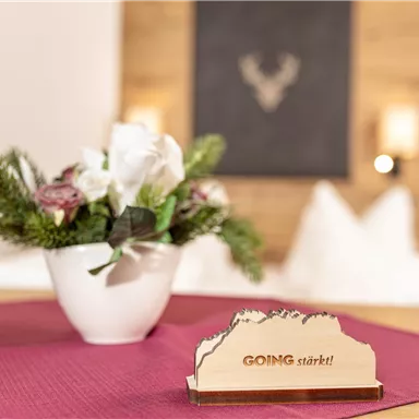 A beautiful table with a blooming plant in a white pot and a decorative wooden overlay with the inscription "GOING starts!". In the background, a modern, cozy atmosphere can be seen.