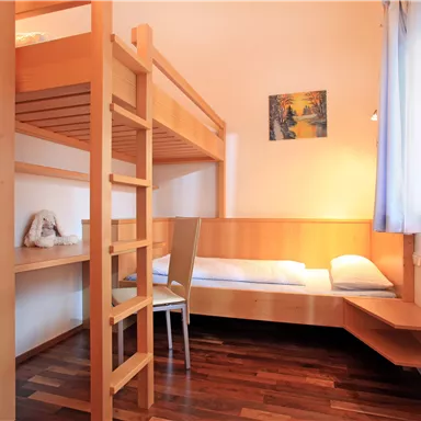 A simple room with a loft bed and a single bed. The walls are light and the light streams through the window.