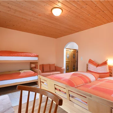 Ein gemütliches Zimmer mit zwei Etagenbetten und einem Doppelbett. Die Wände sind in sanften Farbtönen gestrichen und die Bettwäsche ist in warmen Farben gehalten.