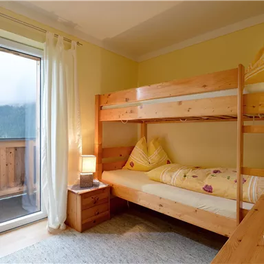 A cozy bedroom with a bunk bed and a large window. The walls are painted in a soft yellow tone, and the room feels bright and inviting.