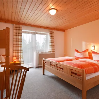 Ein gemütliches Schlafzimmer mit zwei Betten und hellen, orangefarbenen Bettdecken. Das Zimmer hat Holzelemente und große Fenster, die viel Licht hereinlassen.