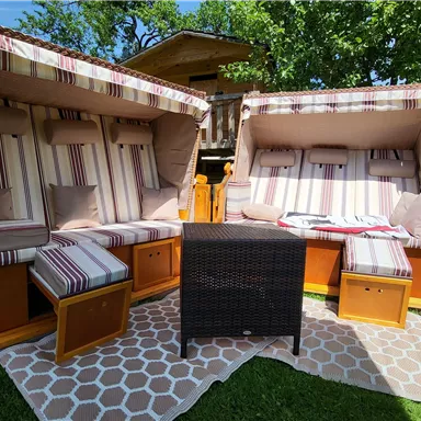 Two cozy loungers with striped cushions are in the garden. A small rattan table complements the relaxed atmosphere.