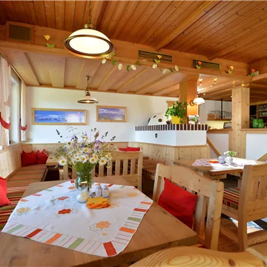 An inviting restaurant with wooden interiors and cozy seating areas. Flower arrangements on the tables and a friendly reception area create a warm atmosphere.