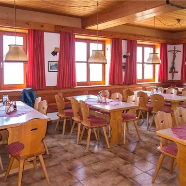 Ein gemütliches Restaurant mit Holzstühlen und Tischen. Die großen Fenster lassen viel Tageslicht herein und die roten Vorhänge verleihen eine warme Atmosphäre.