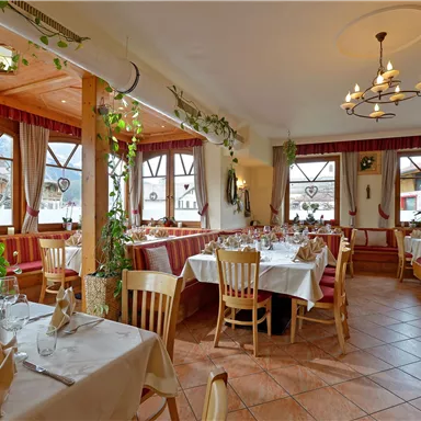 Ein gemütliches Restaurant mit Holzdekor und vielen Fenstern. Die Tische sind elegant gedeckt und umgeben von Pflanzen.