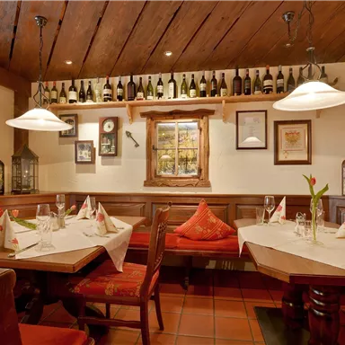Ein gemütliches Restaurant mit Holzdekor und eleganten Tischen. An den Wänden sind Weinflaschen und dekorative Elemente.