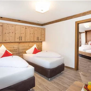 Ein gemütliches Zimmer mit zwei Einzelbetten und traditionellem Holzdesign. Der Raum ist hell und einladend, mit einem offenen Blick auf einen angrenzenden Raum.