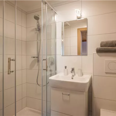 A modern bathroom with a glass shower and a sink. Fresh towels and toiletries are arranged throughout the area.