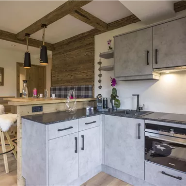 Eine moderne Küche mit grauen Möbeln und einer eleganten Arbeitsplatte. Der Raum hat ein gemütliches Ambiente mit Holzbalken und einem Barbereich.