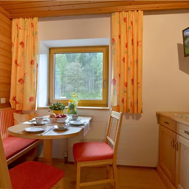 A cozy dining area with a round table and red chairs. The room is bright and has a window with a view of greenery.