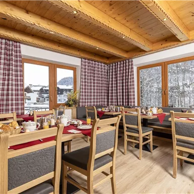 A cozy dining room with wooden tables and chairs. Through the windows, you can see the snowy landscape outside.