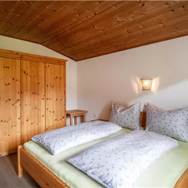 Ein gemütliches Schlafzimmer mit zwei Betten und weißen Bettdecken. Im Raum steht ein Holzkasten und ein kleiner Tisch.