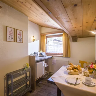 Ein gemütlicher Essbereich mit Holzdecken und natürlichem Licht. Der Tisch ist gedeckt mit Frühstücksgebäck und Blumen.