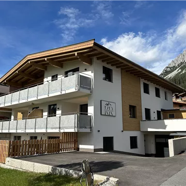 A modern building with wood and stone architecture in the mountains. It has balconies and a beautiful surrounding with green grass.