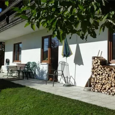 A cozy terrace with chairs and a woodpile. The garden is green and sunny, ideal for relaxing.