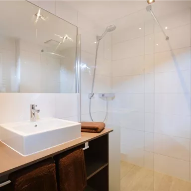 A modern bathroom with a shower and an elegant sink. The walls are brightly tiled, and there is a stylish shelf.