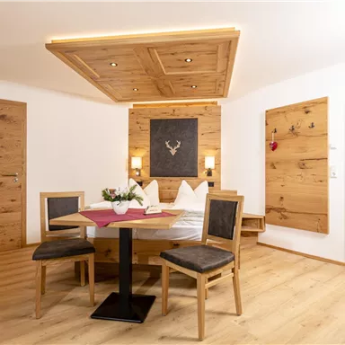A cozy room with wood paneling and modern furniture. The dining table is decorated with a vase of flowers and there is a large mirror on the wall.