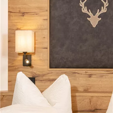 A cozy bedroom with wood decor and a stylish deer antler as wall art. Large, white pillows are on the bed.