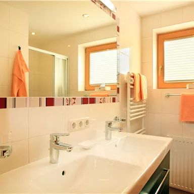 A modern bathroom with a double sink and large mirrors. Bright tiles and orange towels give the room a friendly atmosphere.