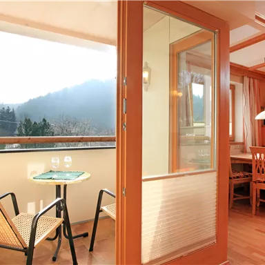 A bright apartment with a balcony overlooking the mountains. The room is modernly furnished with a table and chairs.