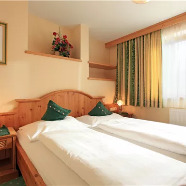 A cozy room with two single beds and a warm atmosphere. The room is decorated with plants and soft curtains.