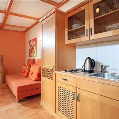 A cozy kitchen corner with wooden furniture and a small seating area. The walls are in warm shades of orange and brown.
