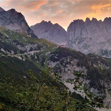 Eine beeindruckende Berglandschaft mit steilen Felsen und üppigem Grün. Der Himmel zeigt sanfte Farben bei Sonnenuntergang.