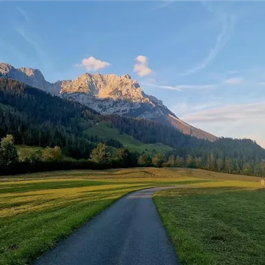 Eine malerische Landschaft mit sanften Hügeln und majestätischen Bergen im Hintergrund. Ein ruhiger Weg führt durch die saftigen Wiesen.