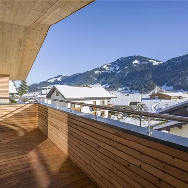 Ein Balkon mit Holzverkleidung und Blick auf schneebedeckte Berge. Der klare blaue Himmel vervollständigt die Winterlandschaft.