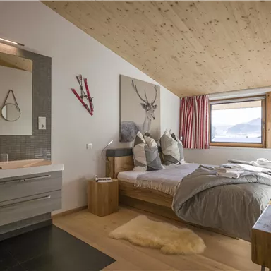 Ein gemütliches Schlafzimmer mit einem Doppelbett und einem modernen Badezimmer. große Fenster bieten einen Blick auf die Berge und lassen viel Tageslicht herein.