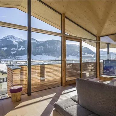 Eine moderne Wohnung mit großen Fenstern und Blick auf schneebedeckte Berge. Der hell gestaltete Raum lädt zum Entspannen ein.