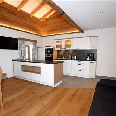 A modern kitchen with wood details and a dining area. The space is bright and welcoming with large windows.