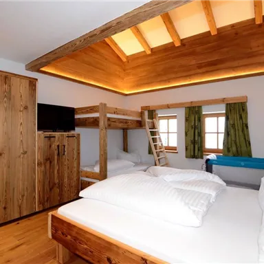 A cozy bedroom with a bunk bed and a large bed. Wooden furniture and a modern style create an inviting atmosphere.