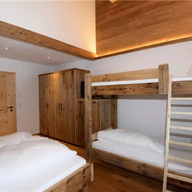 A cozy room with wooden furniture and a loft bed. There is a single bed and a wardrobe, along with a bright atmosphere.