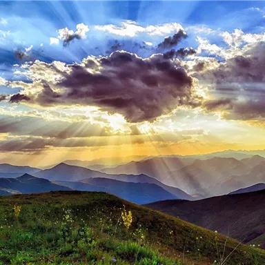 A breathtaking view of green hills under a colorful sky. Sun rays break through the clouds and illuminate the landscape.
