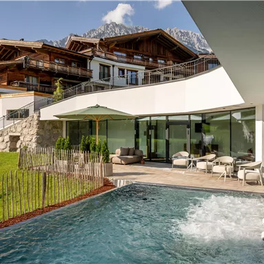 Ein modernes Haus mit einem Pool und einer schönen Gartenlandschaft. Im Hintergrund sind die Berge zu sehen.