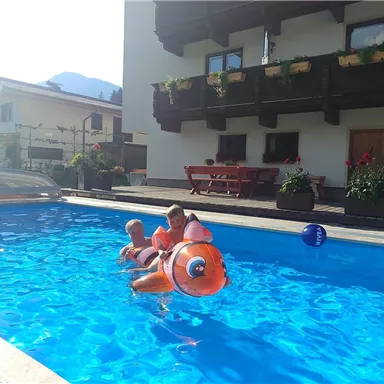 Ein einladender Schwimmingpool mit Kindern, die auf einem aufblasbaren Spielzeug schwimmen. Im Hintergrund sieht man ein charmantes Haus und die umliegende Landschaft.