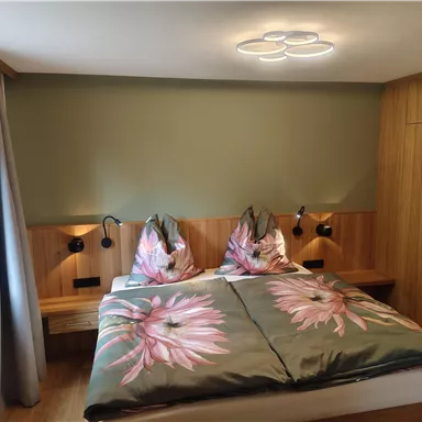 A cozy bedroom with a large bed and floral bedding. The walls are painted in soft tones, and there are modern lighting elements.