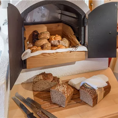A wooden stove with freshly baked bread and rolls. Sliced bread is on a wooden board with a napkin.