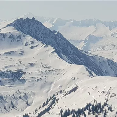 Ein beeindruckendes Bergpanorama mit schneebedeckten Gipfeln. Im Hintergrund sind weitere Berge und eine klare, frostige Atmosphäre zu sehen.