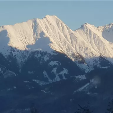 Schneebedeckte Berge unter klarem Himmel. Die majestätischen Gipfel werfen lange Schatten in das Tal.