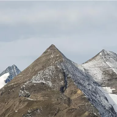 Die Bild zeigt majestätische Berge mit schneebedeckten Gipfeln. Der Himmel ist leicht bewölkt.