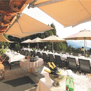 An elegant terrace with tables, surrounded by sun umbrellas and greenery. Ideal for events or relaxed gatherings outdoors.