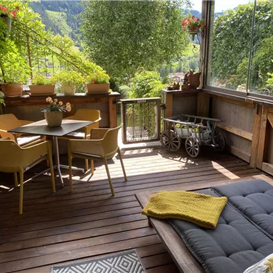 Ein gemütlicher Balkon mit einem Tisch und Stühlen, umgeben von Pflanzen. Im Hintergrund ist eine wunderschöne Landschaft mit Bäumen zu sehen.