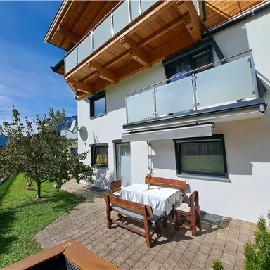 Ein modernes Haus mit einem Balkon und einer Terrasse im Freien. Der Garten ist grün und einladend, ideal für entspannte Momente im Freien.