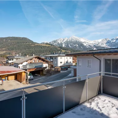Ein wunderschöner Ausblick auf schneebedeckte Berge und eine malerische alpine Landschaft. Die Sonne scheint über die Dächer der Häuser in der Gegend.