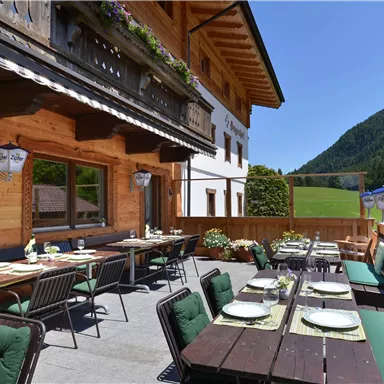 A sunny terrace with a view of the mountains. There are tables and chairs that invite you to dine outdoors.