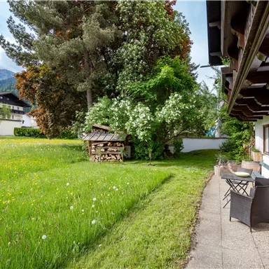 Ein schöner Garten mit grünem Rasen und blühenden Pflanzen. Im Hintergrund stehen Bäume und ein gemütlicher Holzschuppen.