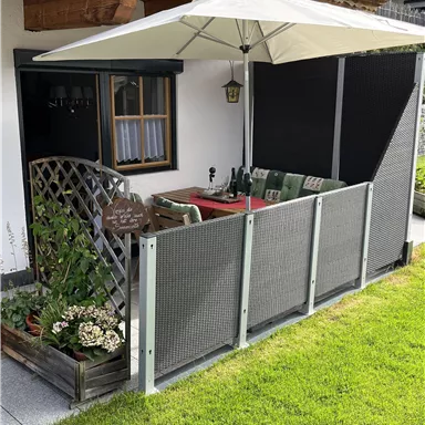 A cozy outdoor area with a sun umbrella and a designated seating corner. The space is green with a small plant box and modern furniture.
