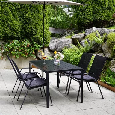 Ein schöner Gartentisch mit Stühlen unter einem Sonnenschirm. Umgeben von grünen Pflanzen und Steinen.